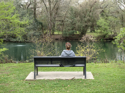 A woman sits on a bench looking towards a pond at Audubon Park, New Orleans, Louisiana, USA.