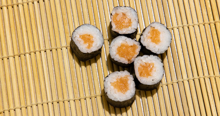 Asia food photography simple background poster concept of maki sushi rolls with salmon wish on traditional Japanese wooden sticks carpet background textured surface and empty copy space