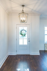 Interior front door entrance with hardwood flooring and a hanging light fixture in a farmhouse style. There are windows on the front door and a wreath hanging with natural light