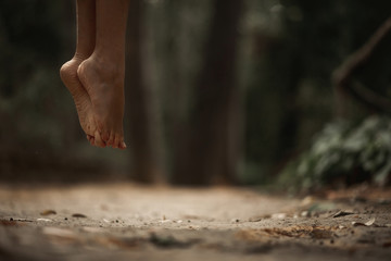 Close up of two barefoot feet of a young woman, floating in midair in the middle of a park. Making...