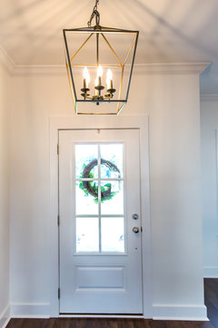 Interior Front Door Entrance With Hardwood Flooring And A Hanging Light Fixture In A Farmhouse Style. There Are Windows On The Front Door And A Wreath Hanging With Natural Light