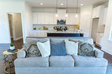 An open concept living room and kitchen with a sofa, end table, and a white cabinet kitchen and island