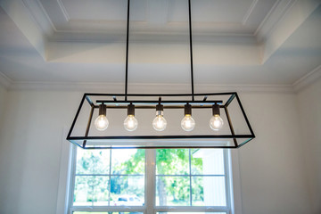 Hanging retro black metal iron chandelier lighting fixture with vintage bulbs hanging in a dining...