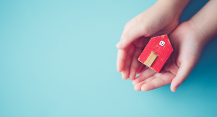 Kid hands holding red home on blue background.Concept for Real estate, Family protection, Stay home Lockdown from Covid-19 Coronavirus. Mortagage Crisis, Relocate Renovate Home.Family safety health.