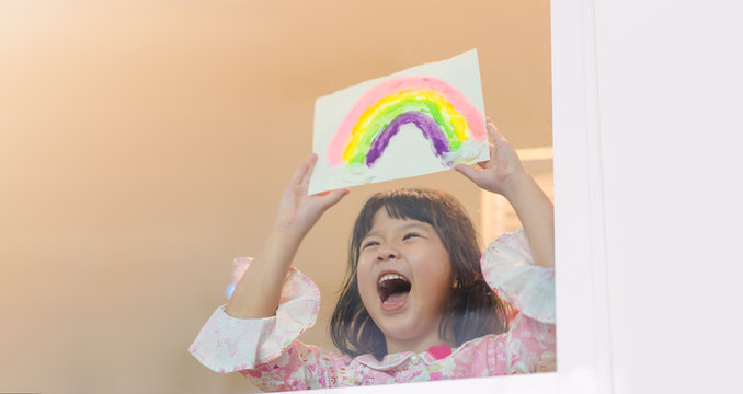 Asian kid home school girl painting showing rainbow during Covid-19 Coronavirus Stay at home for free from Lockdown at home.Social distancing, New normal.Freedom hope during coronavirus covid19.