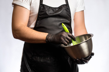 Cropped image of a smiling young male chef or baker man in black apron isolated on gray background. Cooking concept. Beating Eggs in a Bowl