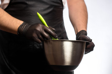 Cropped image of a smiling young male chef or baker man in black apron isolated on gray background. Cooking concept. Beating Eggs in a Bowl