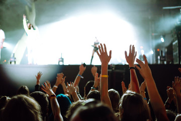 Сrowd with raised hands at music festival. Fans enjoying rock concert with light show and clapping hands.