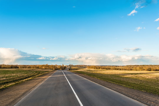 Picture of empty countryside road, horizontal image of a long straight empty highway flanked by green and yellow fields