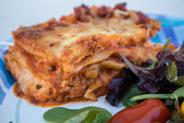 A meal of lasagna and a side green salad on a disposable paper plate