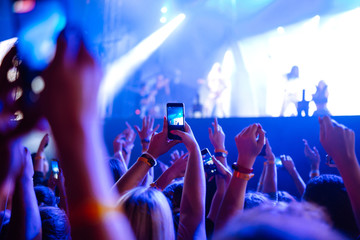 People taking photographs with smart phone during a music festival. Fans enjoying rock concert with...