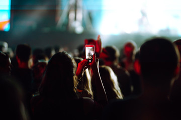 People taking photographs with smart phone during a music festival. Fans enjoying rock concert with light show and clapping hands.