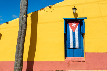 Cuban flag in a blue window with a yellow wall