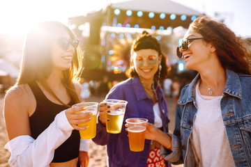 Young girlfriends drinking beer and having fun at music festival. Friendship and celebration. Beach party, summer holiday, vacation concept. 