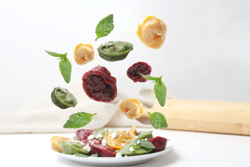 Flying Colorful Ravioli Tortellini Dumplings With Basil Leaves On White Plate. Side View.