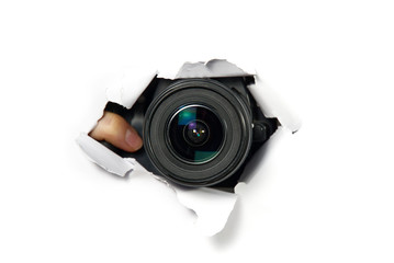 black camera with a telephoto lens that looks out through a hole in white paper. Concept of...