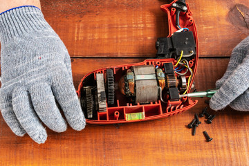 Technician repairs old electric drill on brown wooden table