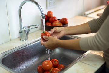 manos lavando tomates bajo el agua de una canilla en la cocina de un hogar