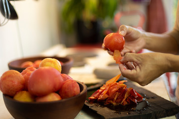 manos pelando tomates frescos sobre tabla de madera con cuenco lleno de tomates pelados
en la...