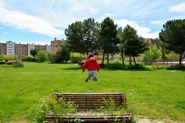 young boy jumping in the park on a bench full of plants