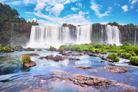 Iguazu waterfalls in Argentina. Panoramic view of many majestic powerful water cascades with mist. Panoramic image with reflection of blue sky with clouds.