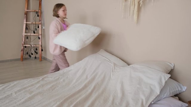 The girl makes the bed, folds the pillows. Side view