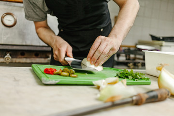 Cook in an apron cutting onions in a restaurant kitchen