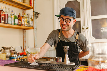 Waiter showing an ice-cold glass with a cocktail prepared at the bar of a modern bar