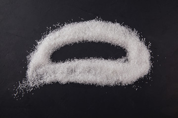 Food additive E621. Powdered crystals of sodium glutamate (Msg) are scattered on a dark background....