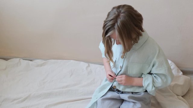 The girl fastens her shirt with buttons and removes the burr from her finger. Side view