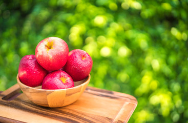 fresh red apples in wooden bowl on a blurred background. Summer garden.