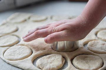 Preparation of the dough for baking, freezing, sculpting and other food blanks - a large piece of the dough is on the table and the chef cuts out small circles on it with an iron shape. Moulding