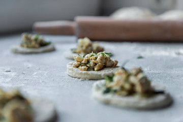 One of the stages of making meat dumplings - on the table on a piece of dough is a meat stuffing with green next to a mound of flour