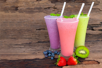 Strawberry  Kiwi and blueberry smoothies colorful fruit juice green purple and red milkshake blend beverage healthy high protein the taste yummy In glass drink episode morning on wood background.