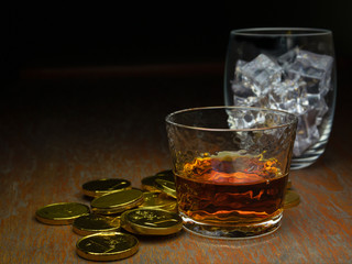 a shot of scotch whiskey, ice cubes and gold coins