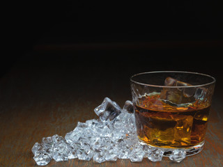 a glass of whiskey on the wooden countertop with ice cubes. A glass of on the rocks or hard liquor served with ice cubes. A shot of spirits, scotch or bourbon.