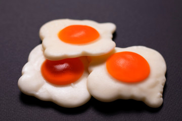Three jelly eggs in the form of scrambled eggs lie on top of each other in the very center on a black background. The photo was taken close-up for your delicious design.