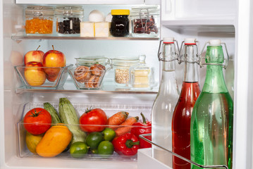 Refrigerador abiero con alimentos y bebidas en recipientes de vidrio, libre de plásticos