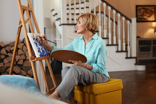 Female Painter. Mature Woman Draws A Painting Using Colour Palette. Indoors Creative Hobby.