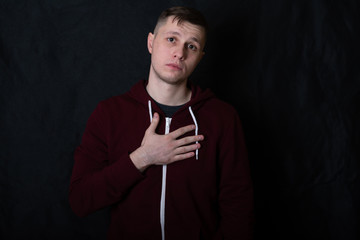 Studio portrait of a young man in a red sweatshirt against black background. A deaf-mute guy shows a 