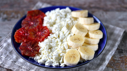 Selective focus. Macro. Plate with cottage cheese with a banana and red orange. Keto diet. Keto dessert. Healthy breakfast or snack.
