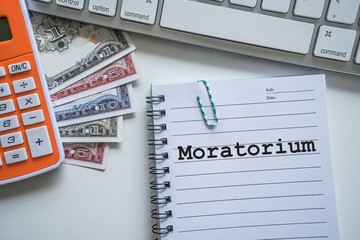 Moratorium (suspension) text with notepad, paper clip, keyboard, calculator and banknotes currency...