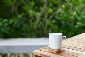 cup of coffee on a wooden table at green tree background