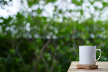 cup of coffee on a wooden table at green tree background