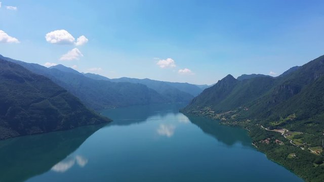 Panoramic view of the mountains and Lake Idro. The reflection in the water of the mountains, trees, blue sky. Flight over the lake