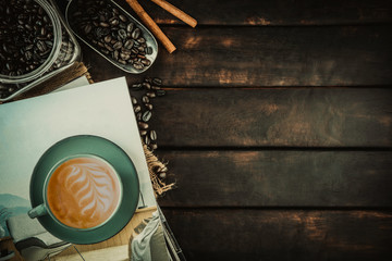latte coffee in a green coffee cup on a book pile above dark grey wooden home kitchen table background