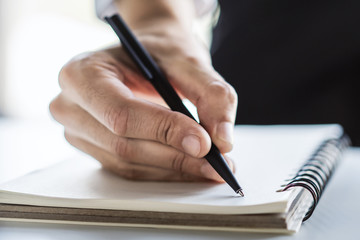 Man writes with a pen in diary in a sunny office, business and education concept. Close up