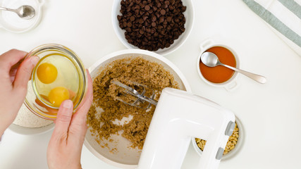 Chocolate Chip Cookies recipe. Chef placing eggs in a bowl, close up on white background, view from above