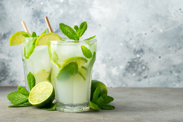 Two homemade lemonade or mojito cocktail with lime, mint and ice cubes in a glass on a light stone table. Fresh summer drink. With copy space.