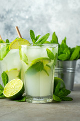 Two homemade lemonade or mojito cocktail with lime, mint and ice cubes in a glass on a light stone table. Fresh summer drink.